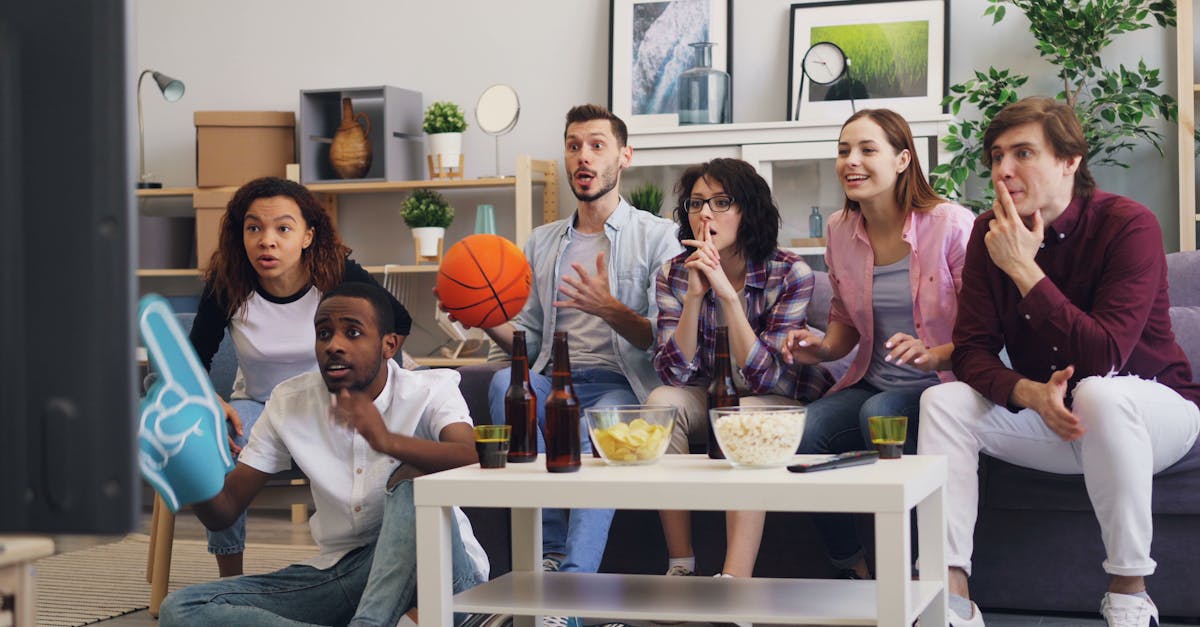 Group of friends excitedly watching a sports game indoors, enjoying snacks.