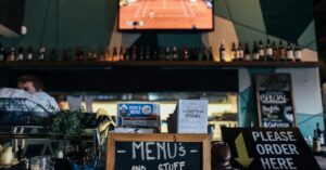 A lively bar scene with menus and bottles, featuring a TV showing sports.